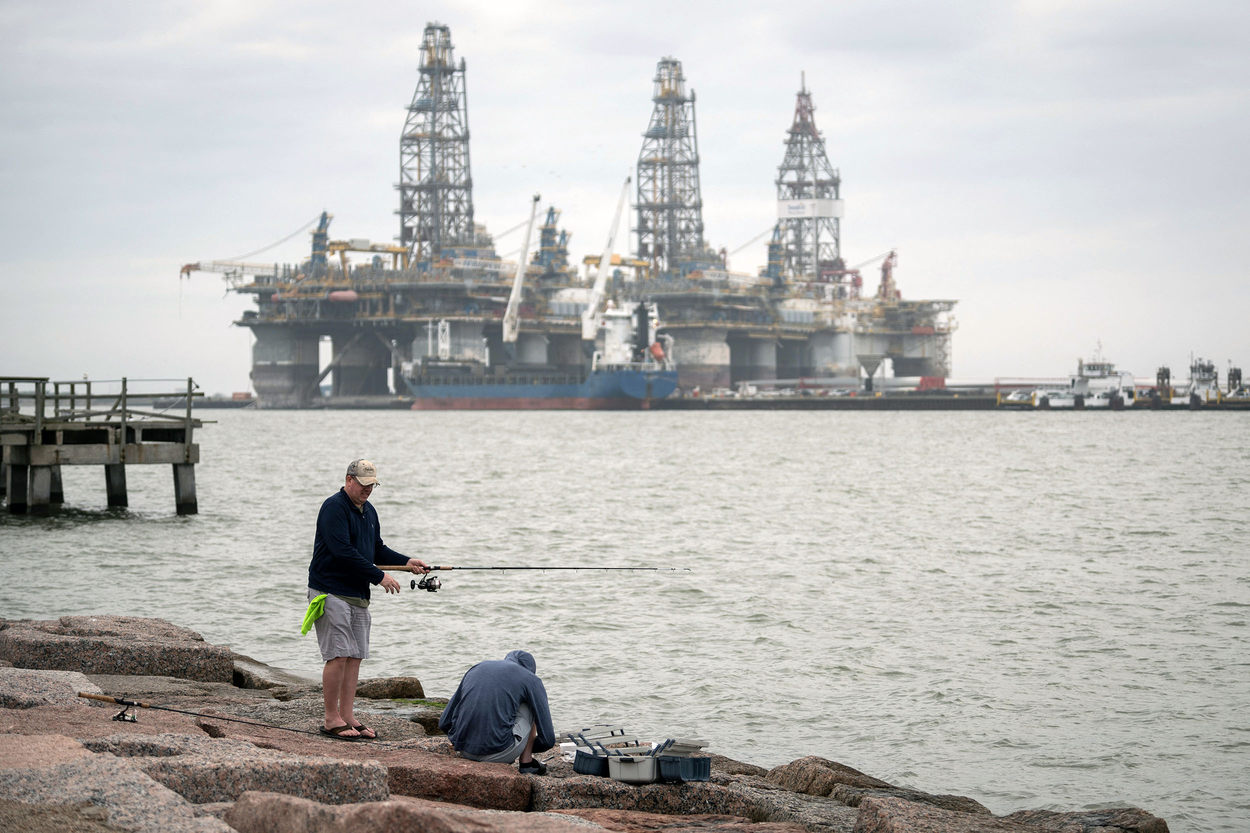 People fish in front of defunct oil drilling rigs in the Corpus Christi Ship Channel at Aransas Pass on March 11, 2019, in Port Aransas, Texas. - To realize America's soaring energy export ambitions, the port of Corpus Christi in Texas is pulling out all the stops: giant new oil pipelines, terminal expansions and undersea construction at considerable environmental costs. (Photo by Loren ELLIOTT / AFP)