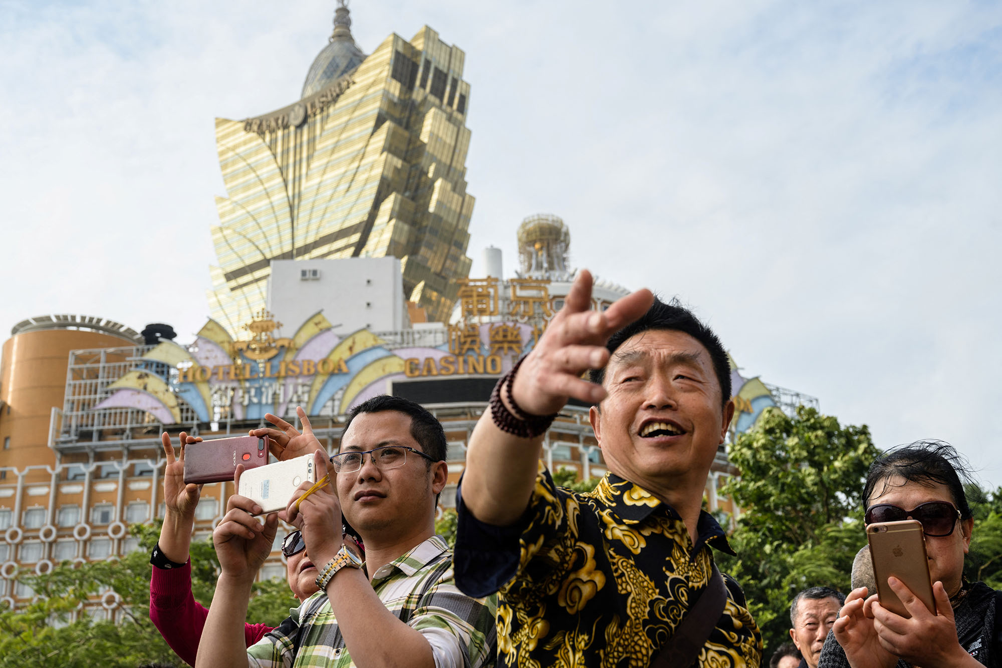 In this photo taken on March 5, 2019, visitors take photos near the Grand Lisboa (back C) casino resort in Macau. - The trade war may have sent ripples of uncertainty through the world's second-largest economy but one corner of China has so far remained steadfastly buoyant -- the gambling enclave of Macau. (Photo by Anthony WALLACE, AFP)